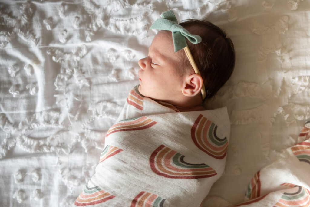 Lifestyle newborn photo of baby in swaddle on white bed