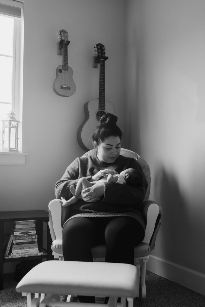 Black and white image of Mom sitting in rocking chair in nursery, holding newborn son. The nursery has a music theme with guitars hanging on the walls behind them.