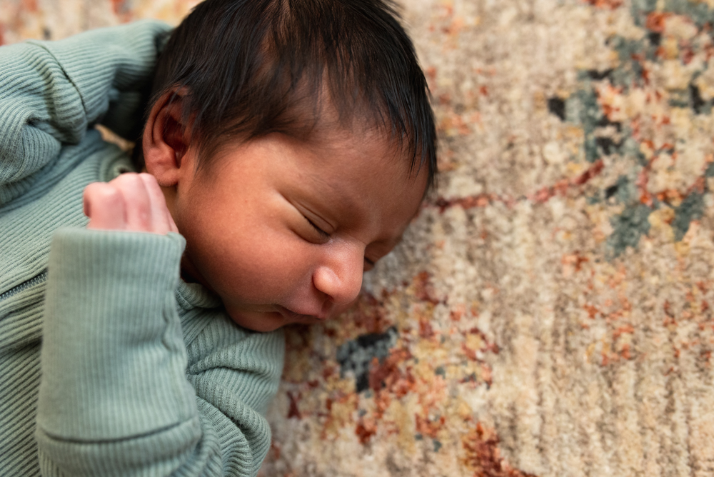Newborn baby lying on a colorful rug during a relaxed lifestyle newborn photography pose at home