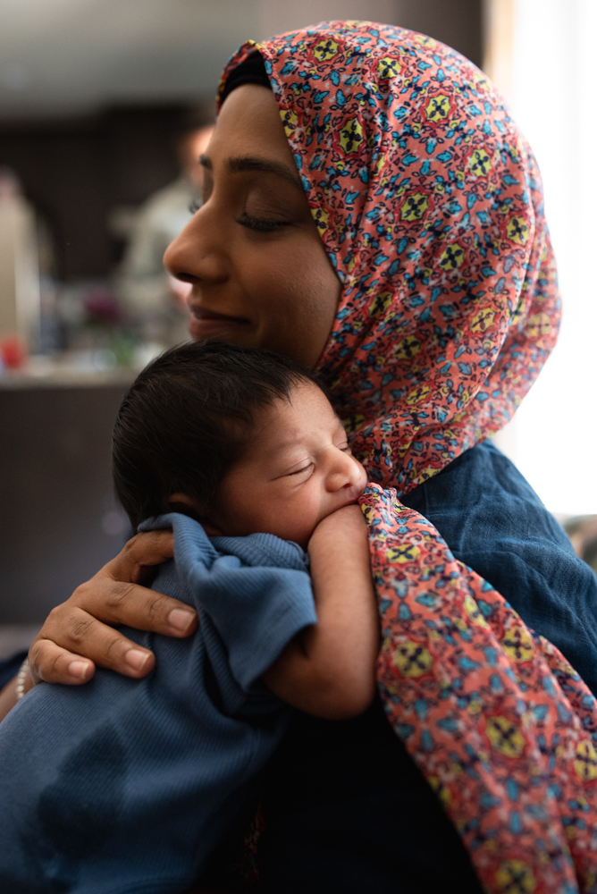 Mother cuddling her newborn close during a warm lifestyle newborn photography pose in natural light