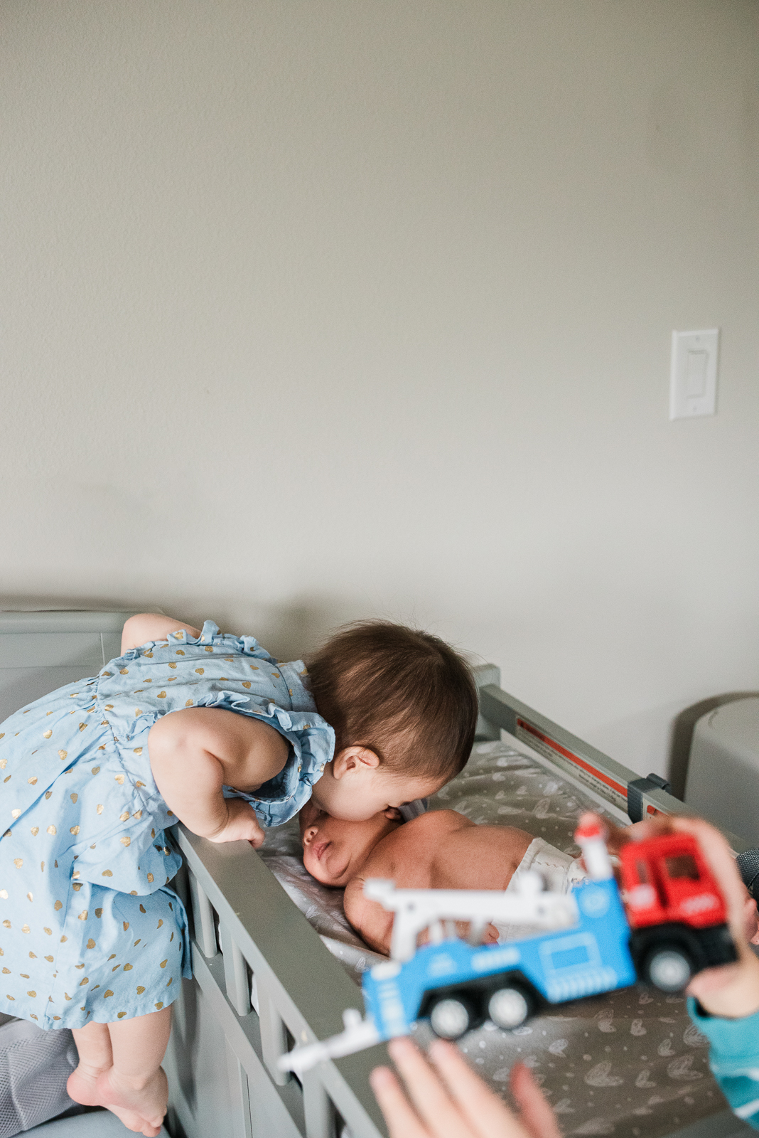 Toddler in crib leaning over to kiss baby sister on the cheek