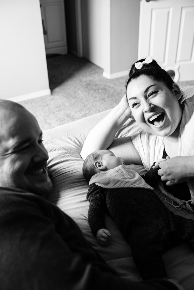 Authentic in-home family moment with parents laughing with their baby on the bed